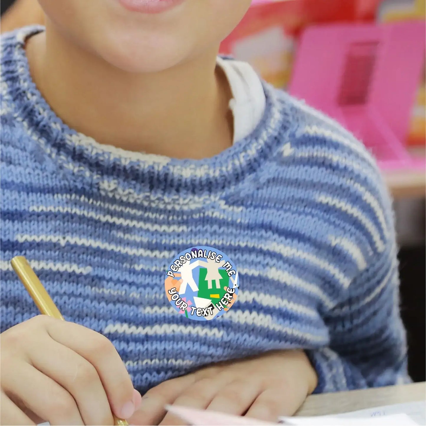 Child in classroom wearing customizable reward sticker, writing with pencil