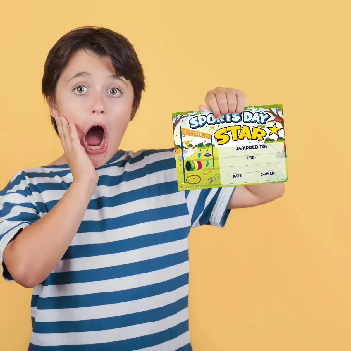 Excited child holding sports day star award certificate, striped shirt, yellow background