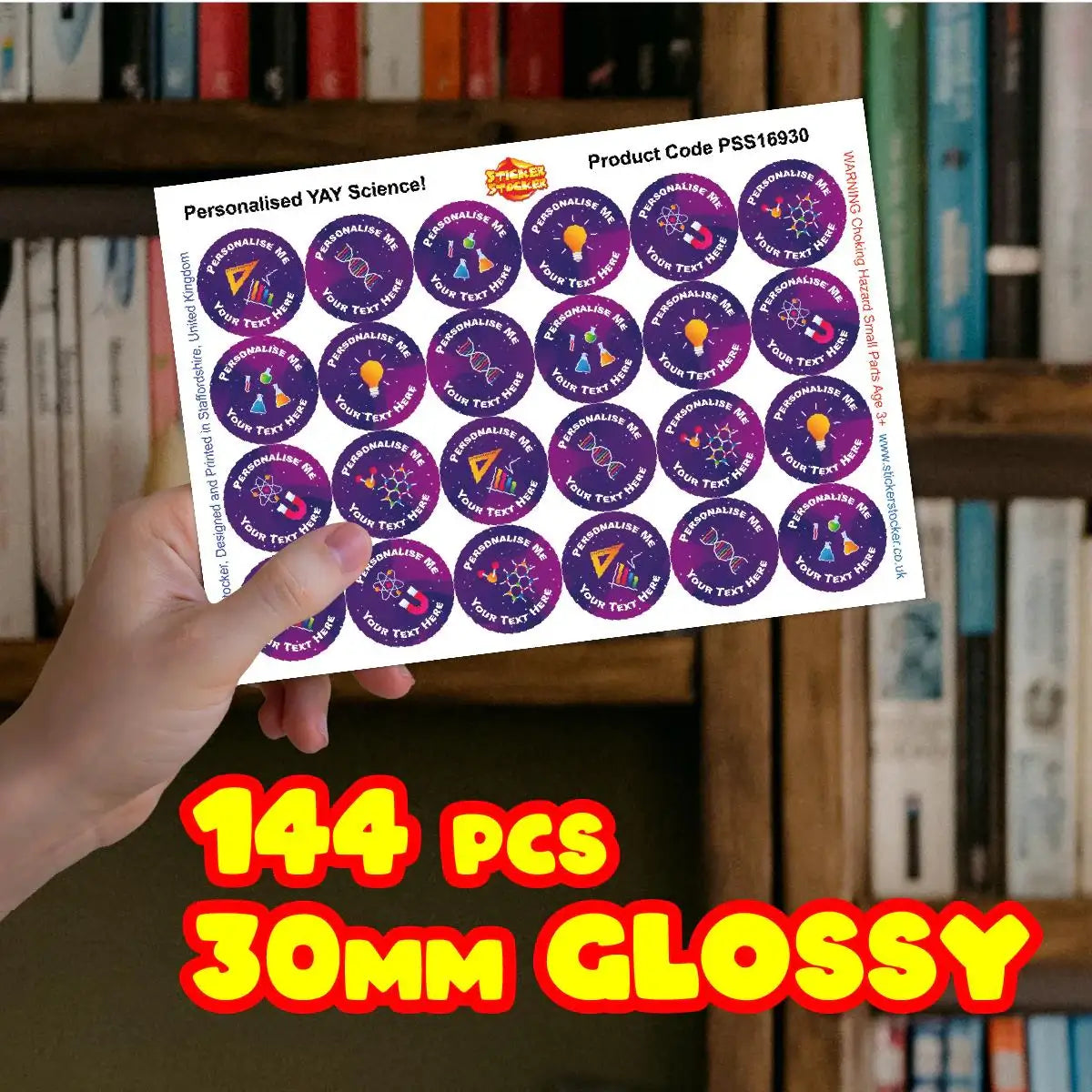 Hand holding sheet of 30mm glossy science reward stickers, 144 pieces, in front of bookshelf.