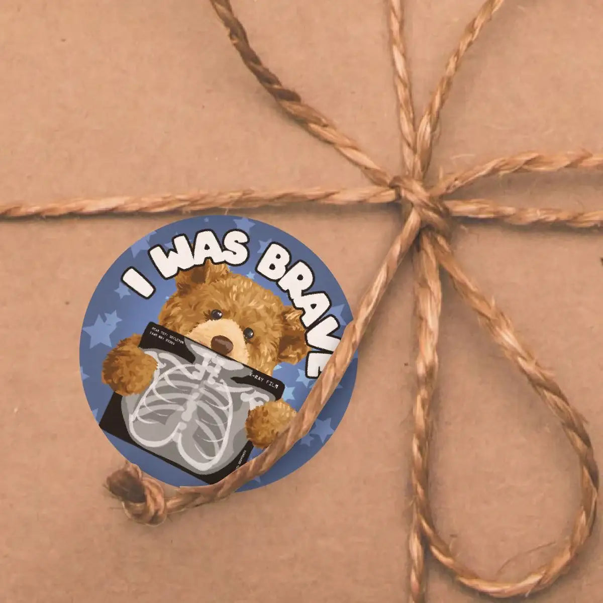 Round reward sticker with a teddy bear holding an X-ray, text reads 'I Was Brave', on kraft paper.