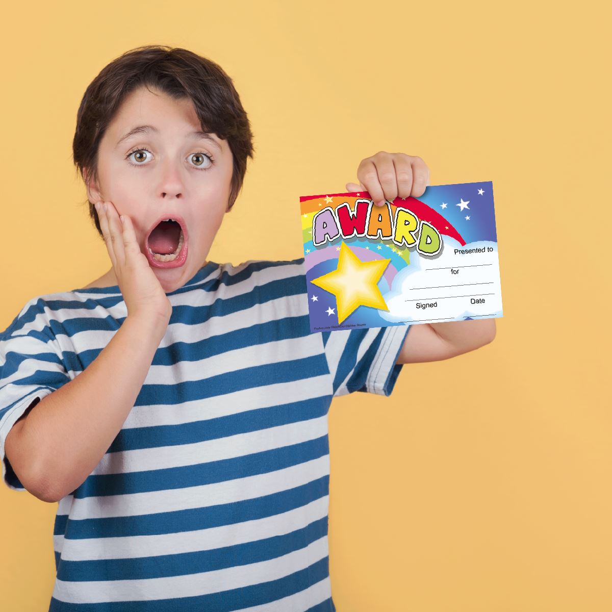 Surprised child holding colorful classroom award certificate against yellow background