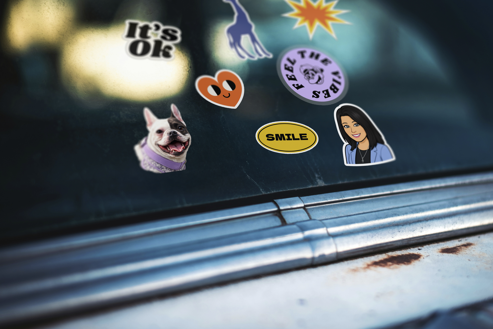 A close-up of several colorful stickers applied to a dark car window above a chrome trim strip. The stickers include a black-and-white dog face, a purple circular graphic, a heart-shaped orange symbol, a yellow oval with the word 'SMILE', a portrait sticker, and other abstract designs.